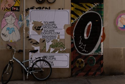 Urban street wall with graffiti art and torn mockup posters next to a parked bicycle, representing real-life mockup templates for designers.